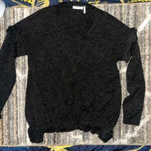 This is a black sweater with ruffles at the top of the sleeve.